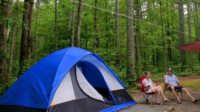 Two campers sitting in relaxing in folding chairs outside their tent.