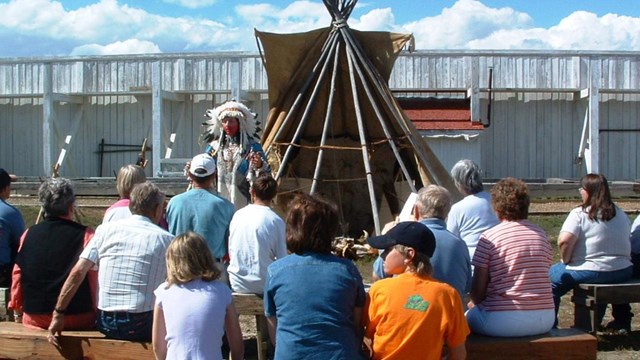 American Indian Interpreter in full regalia speaking to seated visitors.