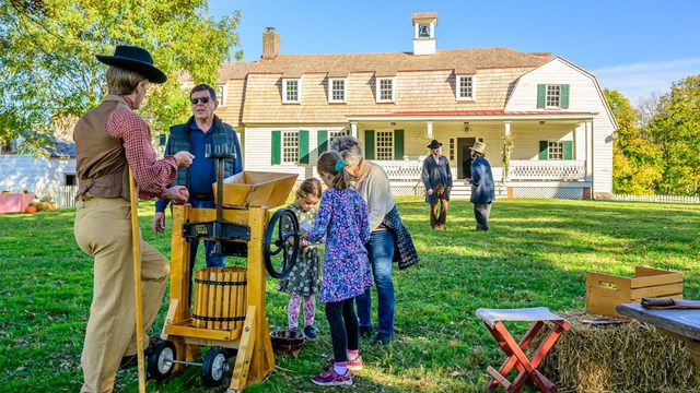 A family of modern visitors talking to a costumed ranger outside of the lower house