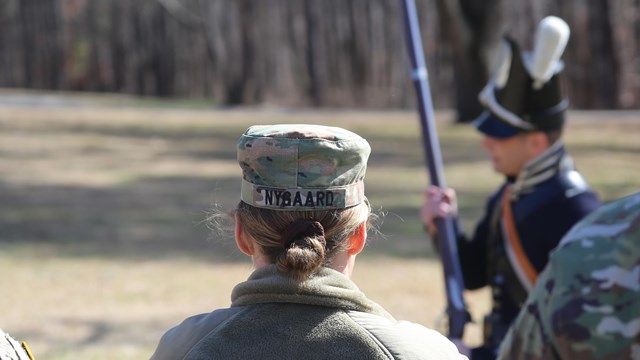 military personnel in foreground looking away from camera at living history demonstrator with musket