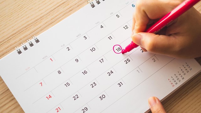 Female hand circling a date on a calendar, with a marker. 