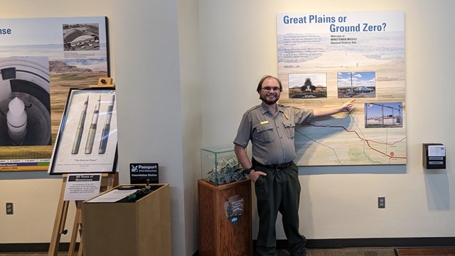 Man in gray shirt and green pants pointing on a large map on the wall