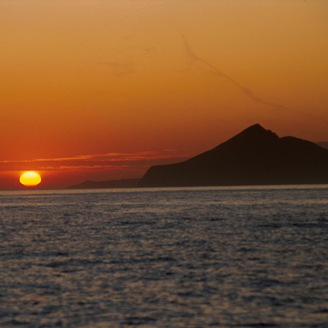 sunset setting over ocean with mountain silhouette.