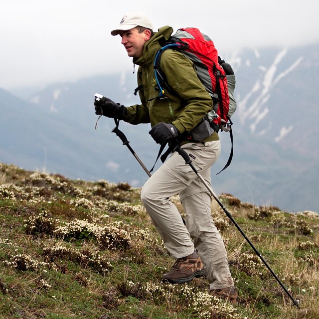 Hiker with poles, backpack, and winter coat on a mountain trail