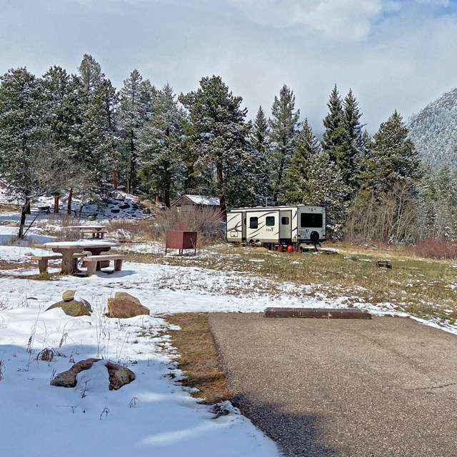 A view of a campsite in Aspenglen Campground with an RV parked. The campsite has snow on the ground