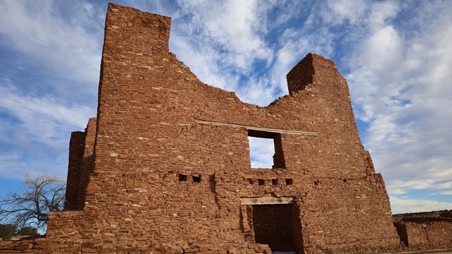 Red sandstone church ruins against a cloudy blue sky.