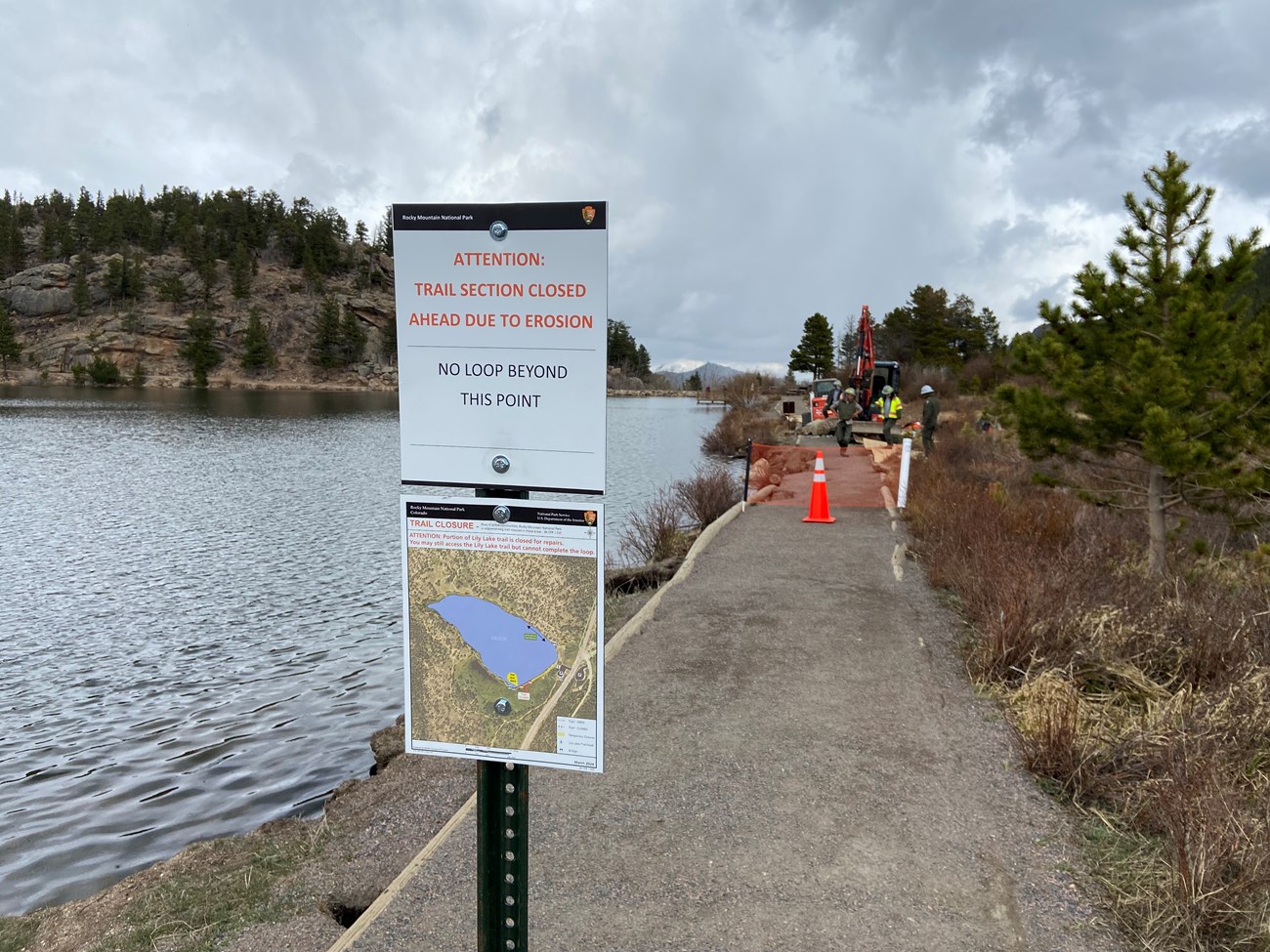 A sign is posted for the Lily Lake Trail Closure. NPS staff are using a bobcat and other equipment to repair the trail.