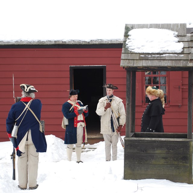 Soldiers stand in snow outside a farm house