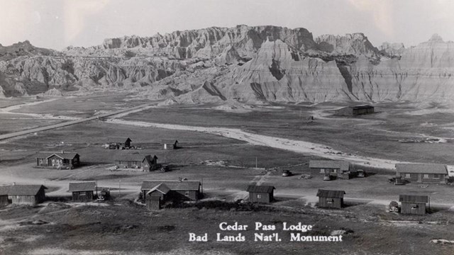 a historic black and white photo of a lodge and cabins in front of badlands buttes.