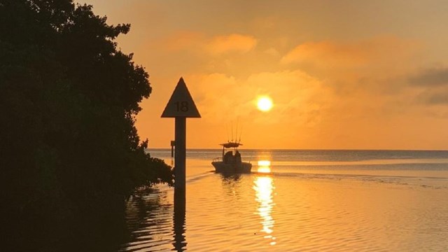 Silhouette of a boat heading out on the water into a glowing orange sunrise