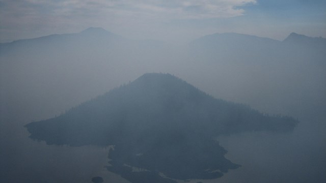 The Crater Lake Caldera is filled with smoke obscuring Wizard Island. 