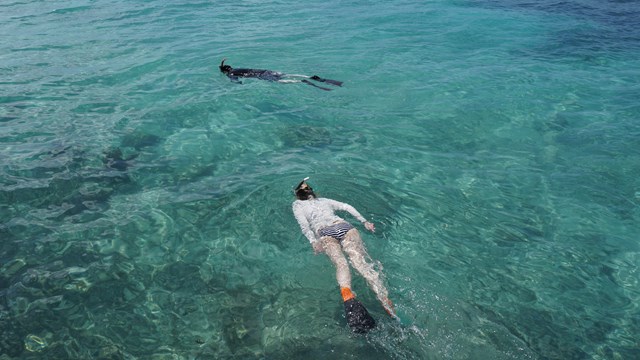 two people swimming in the ocean next to a brick walkway