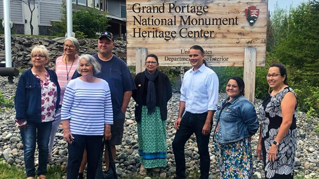 Eight people standing in front of the NPS Monument sign.