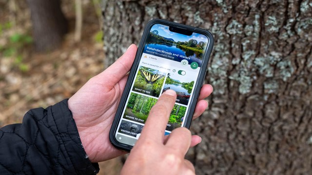 A close up photo of a person navigating the Katahdin Woods and Waters NM Page on the NPS App.