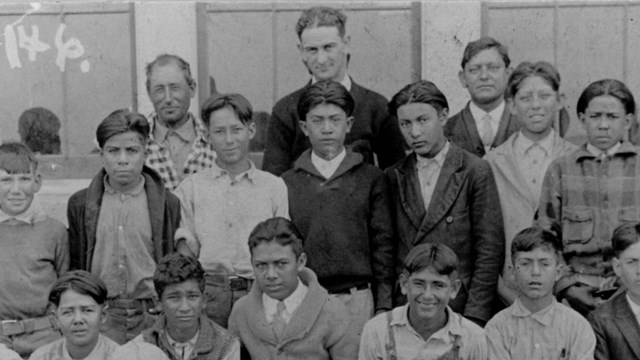 a B&W photo of young students posing with a young President Johnson standing in the back