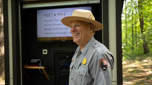 A smiling ranger stands in front of an outdoor screen