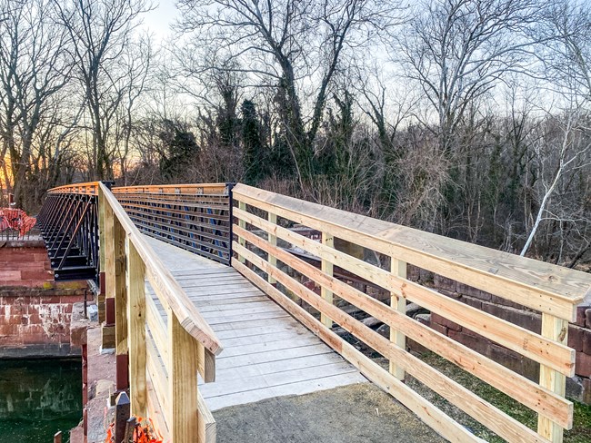 A wood and metal pedestrian bridge spans a portion of a stone aqueduct.