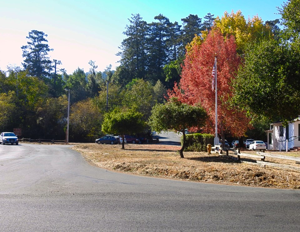 A black and white photo of dirt driveway passing over a cattle guard. Painted on white fences on both sides of the driveway is "Private Entrance. Bear Valley Ranch." Beyond the cattle guard are a number of white buildings, beyond which are tall trees.