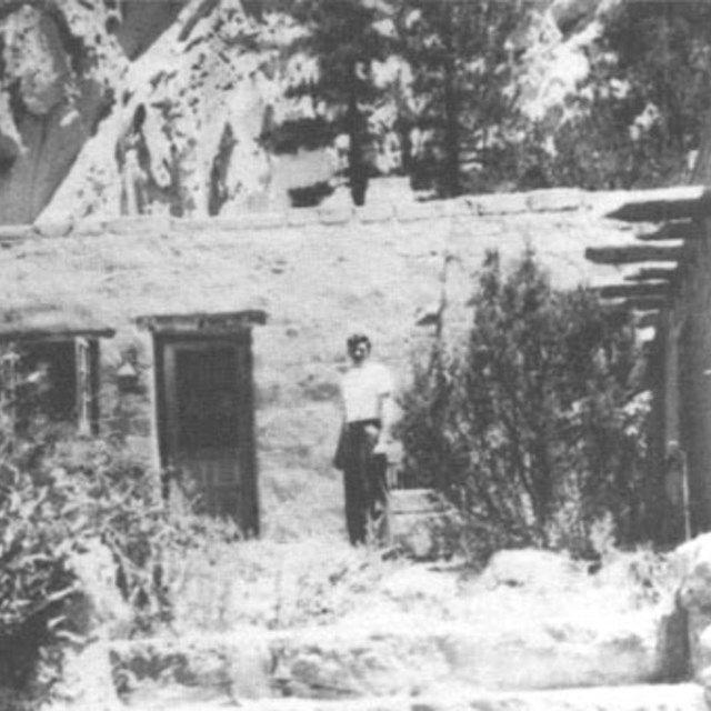 A black and white image of a man standing in front of a strone building.