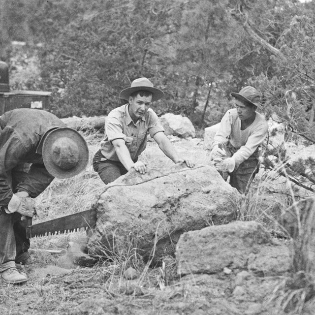 A black and white image of three men cutting a boulder with a handsaw.