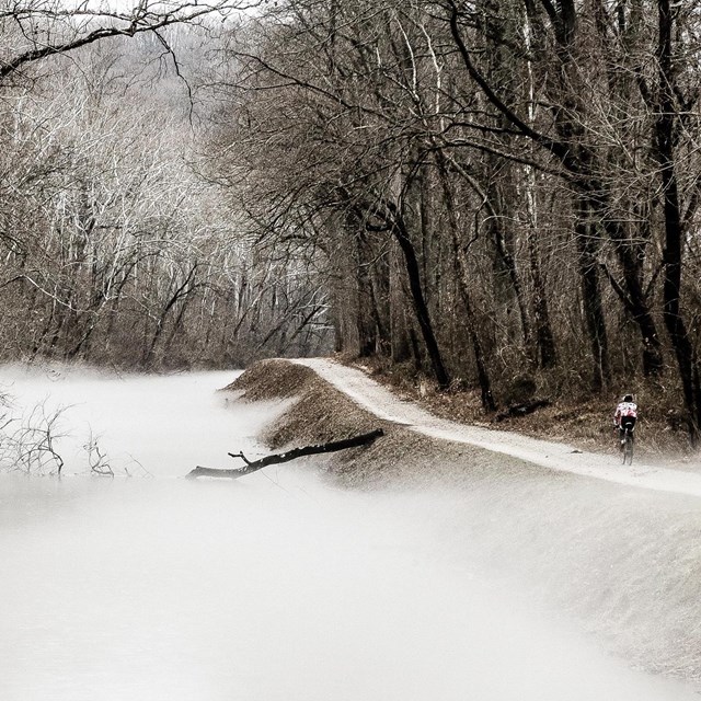 A biker rides along a mist filled canal.