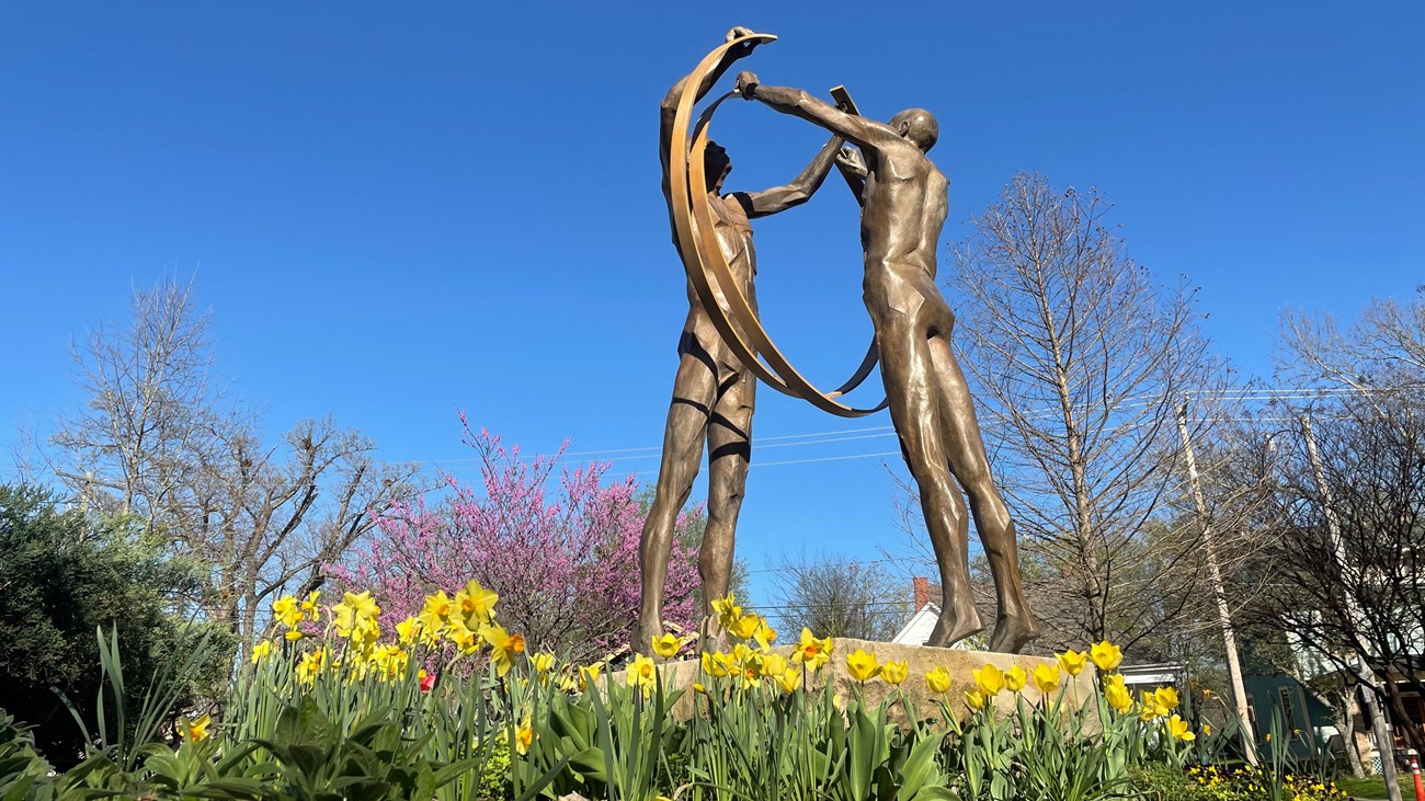 Allegorical statues raise their arms to interlock their respective rings in the effort to be United