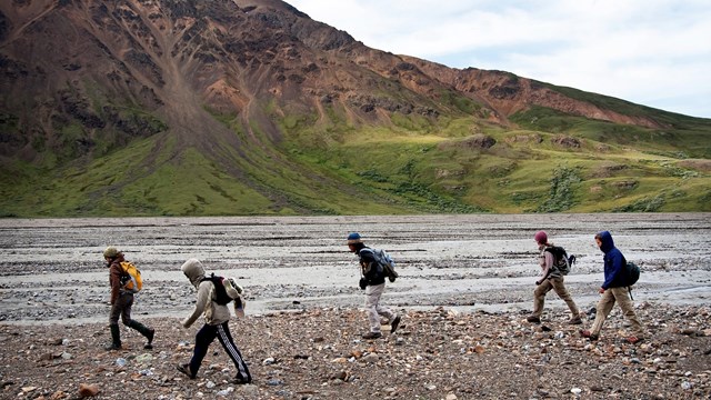 a group of young visitors hike along a gravel riverbank