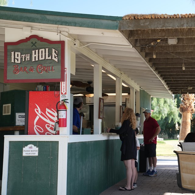 Photo of people sitting down, eating and ordering at the outdoor 19th Hole restaurant