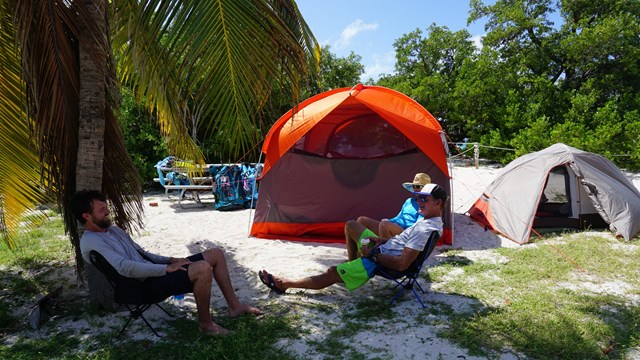 People sitting on chairs beside tents on a beach 