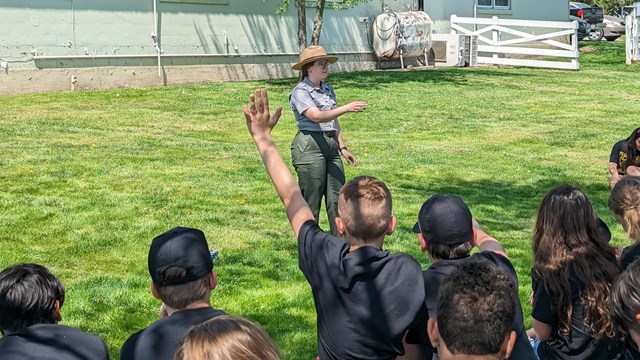 A color image of a park ranger speaking to a group of students wearing matching shirts