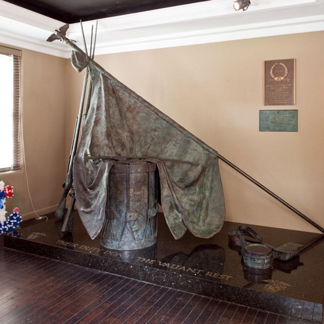 Color photo of bronze sculpture of drum draped by flag.