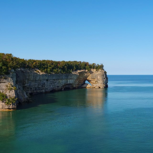 A rocky cliff juts into Lake Superior on a calm day.