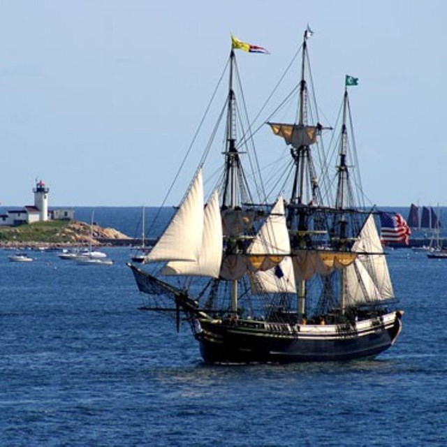 A large three-masted ship sailing on blue waters on a cloudless day.