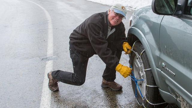 A man installs chains on his vehicle. Photo by Kirke Wrench.