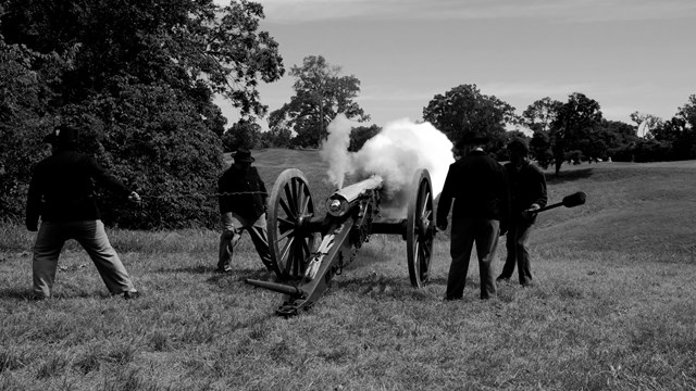 A black and white image of living history staff members firing a cannon.