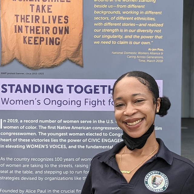 A volunteer smiles in front of a banner sign.