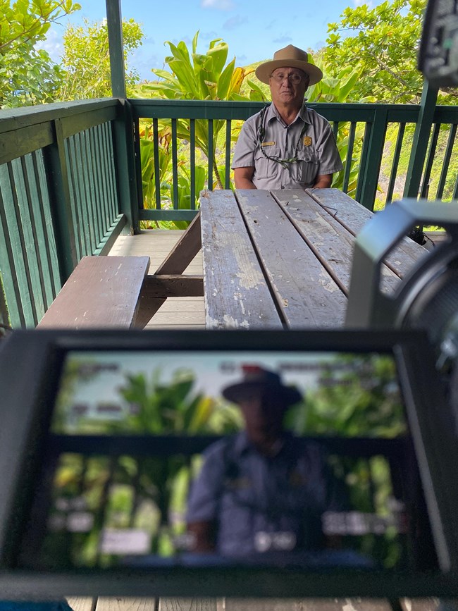 a ranger sits at a picnic table, video camera in foreground