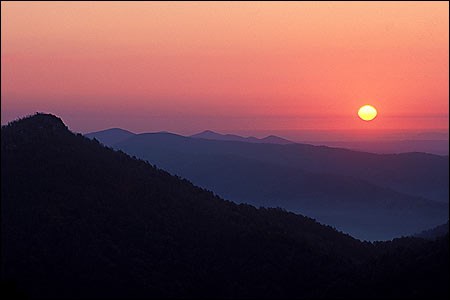 A very vivid pink, purple, and blue sunset over the rolling hills of the Ouachita Forest.