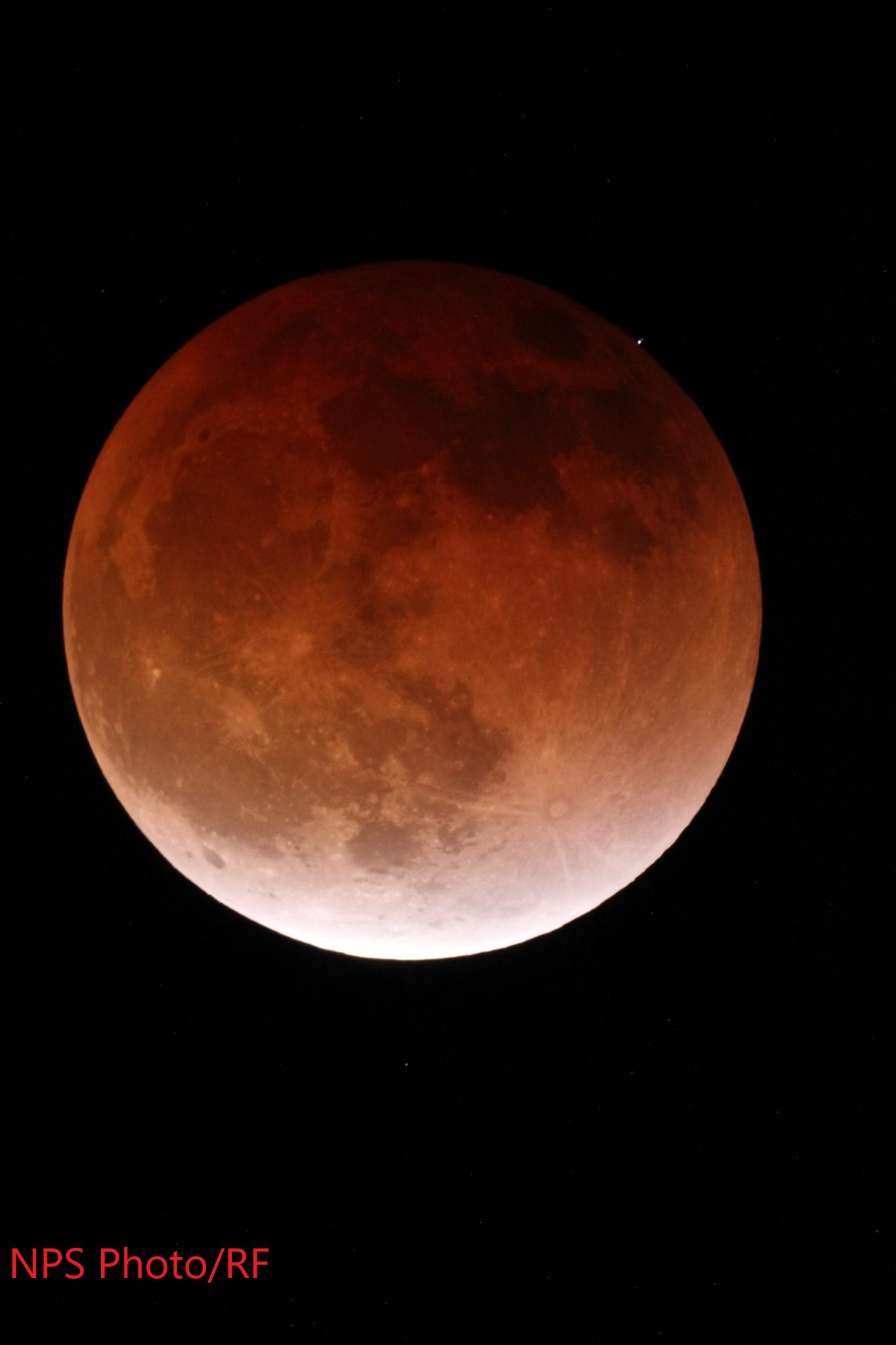 The eclipsed moon appears as an orange circle, seen against the black background of the sky.