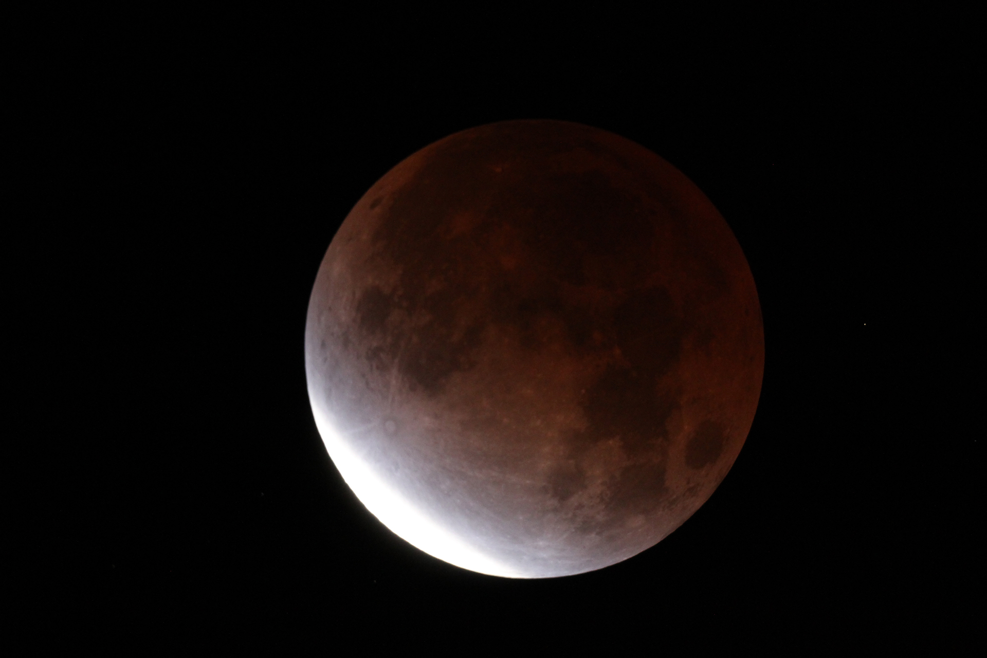 An image of the moon, reddened by Earth’s shadow.  A small area is bright.