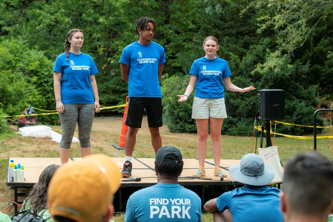 Three youth on an outdoor stage presenting their projects