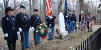Seven men dressed in Civil War Union uniforms stand on each side of grave of Nancy Hanks Lincoln. Two men hold flags, American and State of Indiana. Two ladies place a wreath alongside other wreaths.