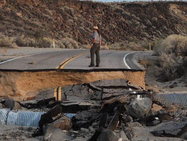 Park ranger standing on top of a paved washed away road.