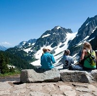 Hikers rest on a bench with mountain views.