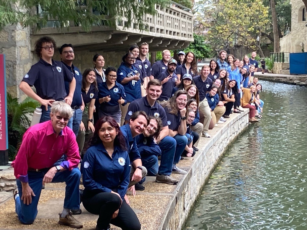 A large group poses for a photo along a rivers edge