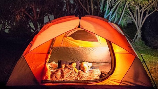 a person lays in a lit up orange tent with the starry night above