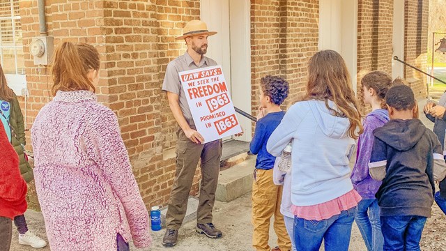 Park ranger with a group of students in front of brick building