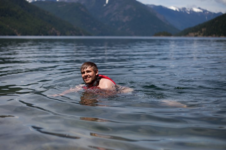 Young man swimming with a life jacket on.  He is smiling and enjoying the lake.
