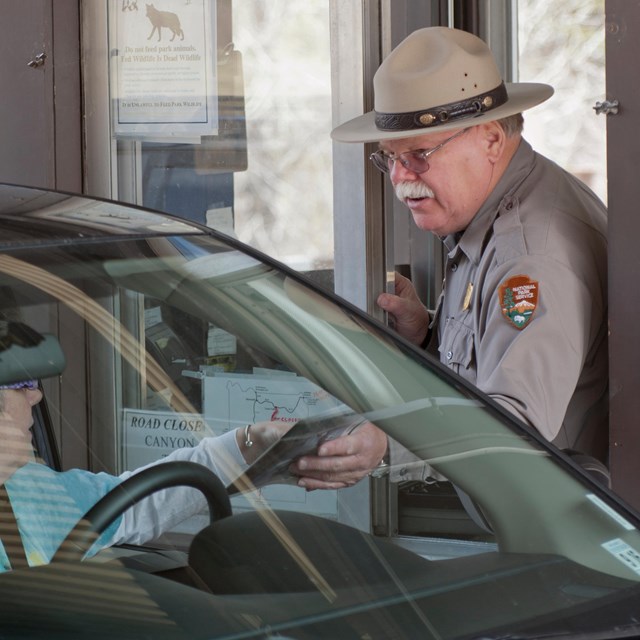 A Park Ranger greets a visitor in a car at the entrance station