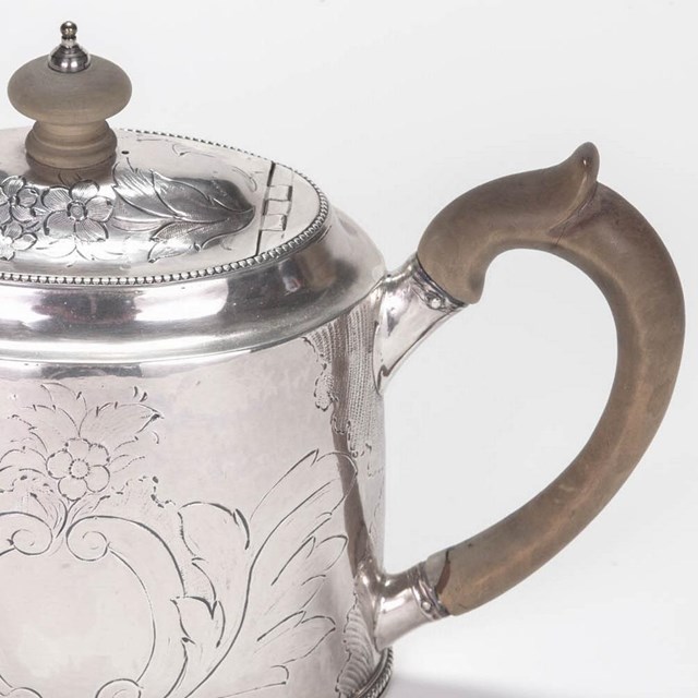 A silver teapot with wood handle.